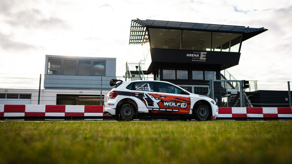 Low shot des Rallyeautos mit dem Start- und Zielturm der Arena E im Hintergrund vor hellem, bewölkten Himmel.