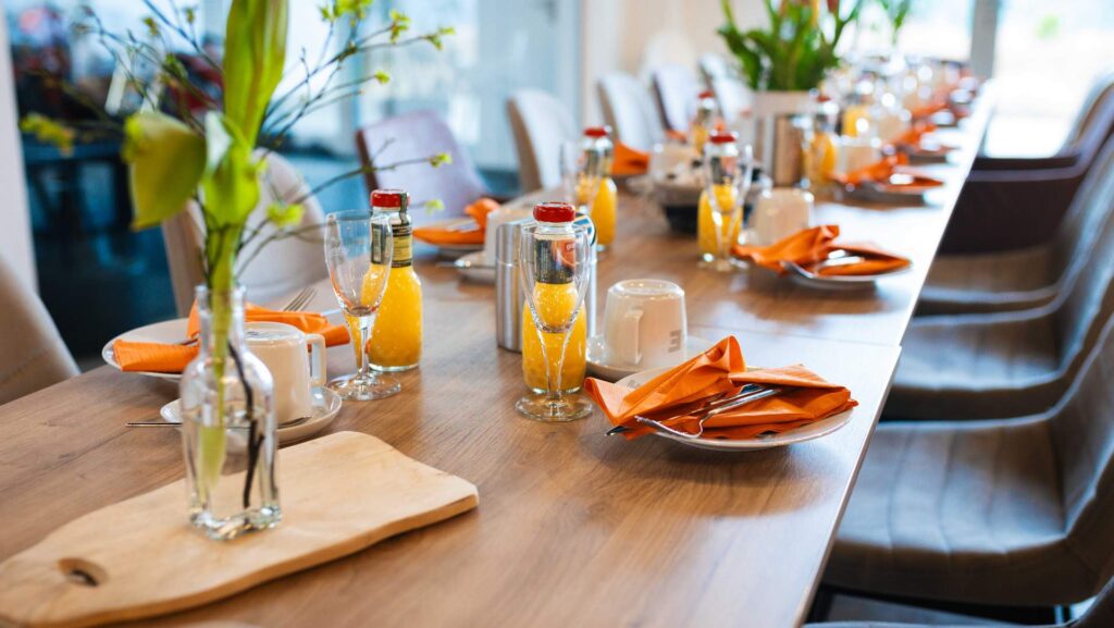 Ein Tisch mit Gläsern, Tischdeko, Saftflaschen und tellern mit orangefarbenen Servietten